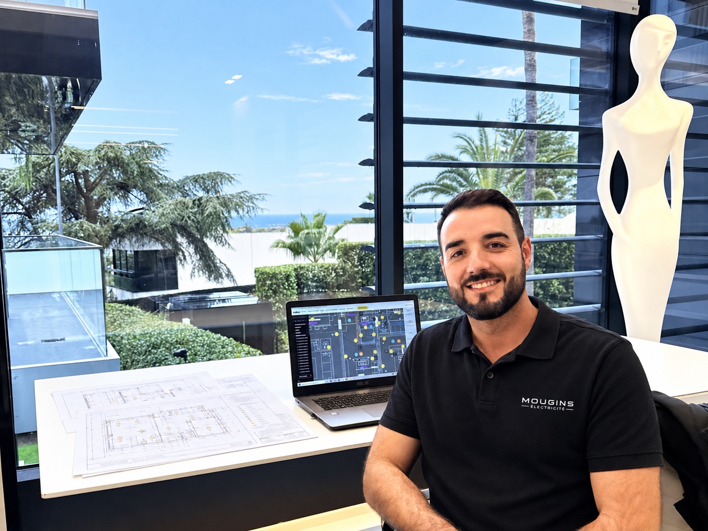 Hugo Montagné, dirigeant de Mougins Électricité, dans son bureau avec des plans électriques